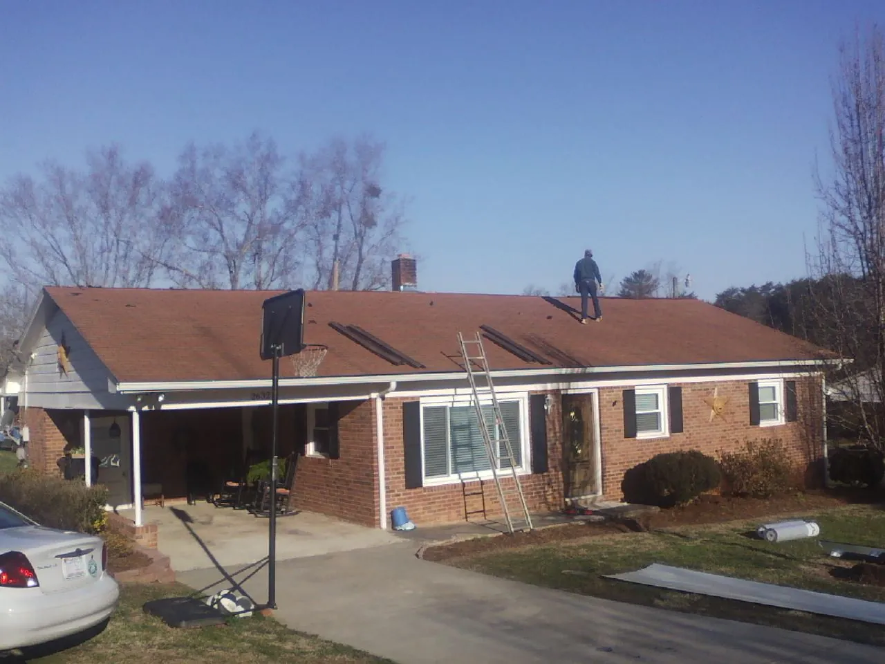Roofer stripping a shingle roof on a brick ranch before metal panels in Monroe
